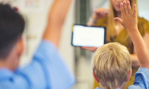 Pupils with hands up answering question on teachers tablet