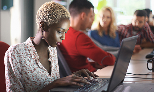 women in meeting room with others working on laptop
